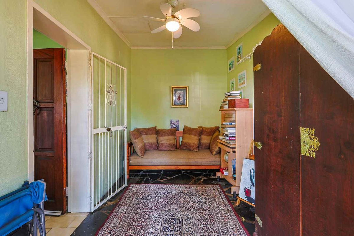 A small interior living space featuring a ceiling fan, stone flooring, and a security gate leading to an adjacent room.
