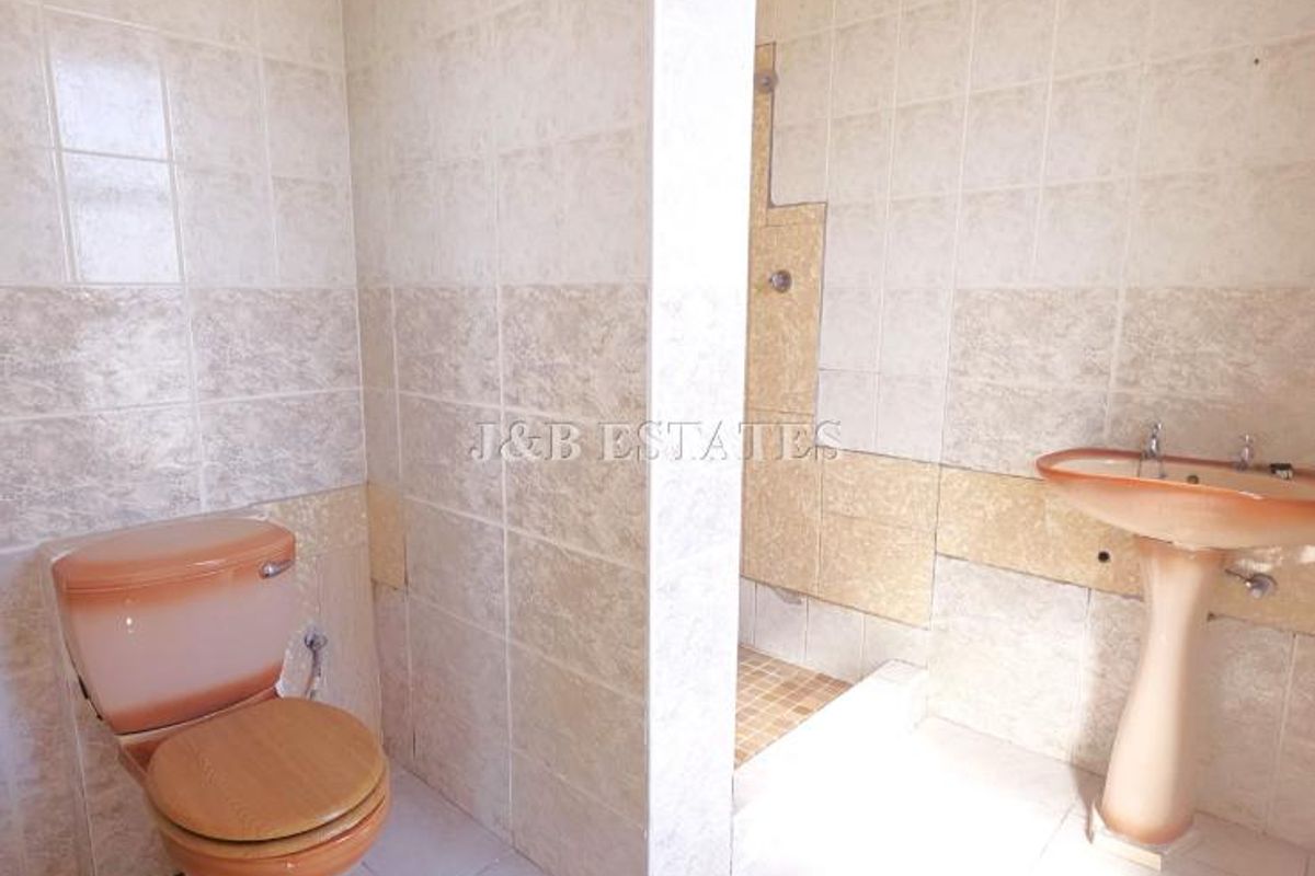 A dated bathroom featuring a pedestal basin, toilet, and a walk-in shower enclosure with tiled walls and flooring.