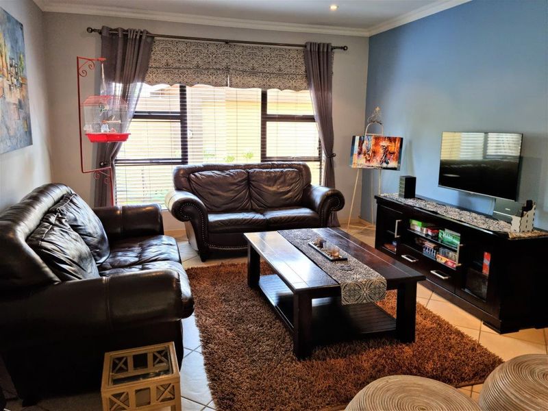 A comfortable living room featuring tiled flooring, large windows with venetian blinds, and a feature wall, providing a functional and inviting space.