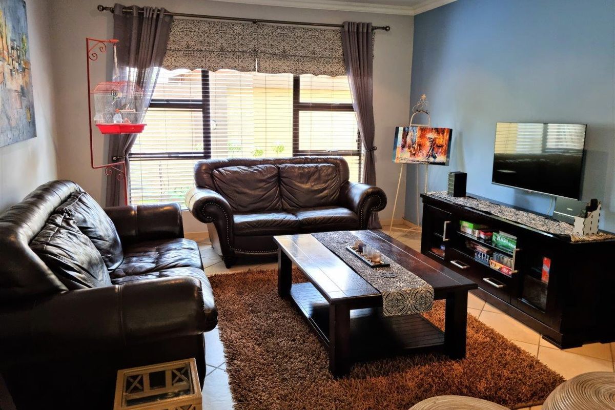 A comfortable living room featuring tiled flooring, large windows with venetian blinds, and a feature wall, providing a functional and inviting space.