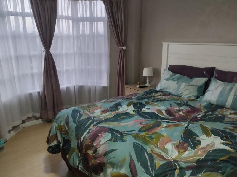 A comfortable bedroom featuring a large bay window that allows for natural light and laminate flooring throughout.