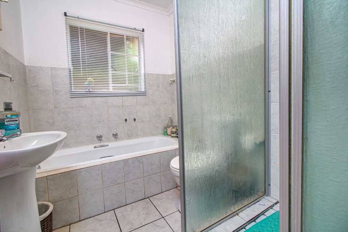 A functional bathroom featuring a tiled bathtub, pedestal sink, and a separate shower enclosure with textured glass doors.