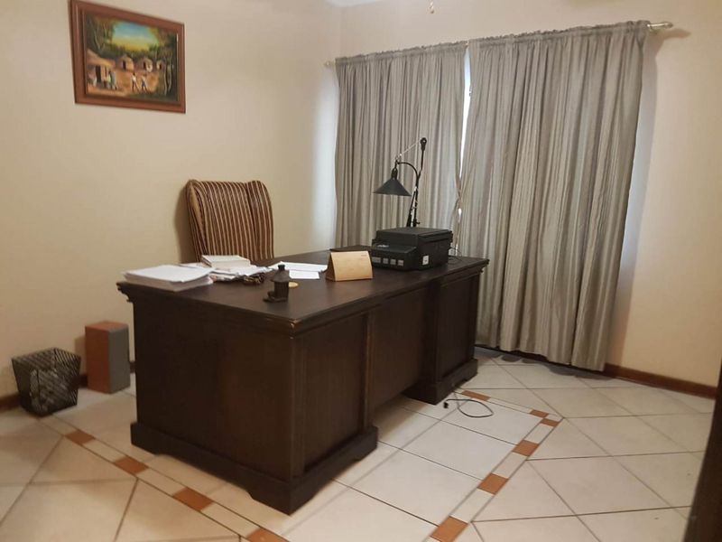 A functional home office space featuring tiled flooring and window treatments, providing a quiet area suitable for work or study.