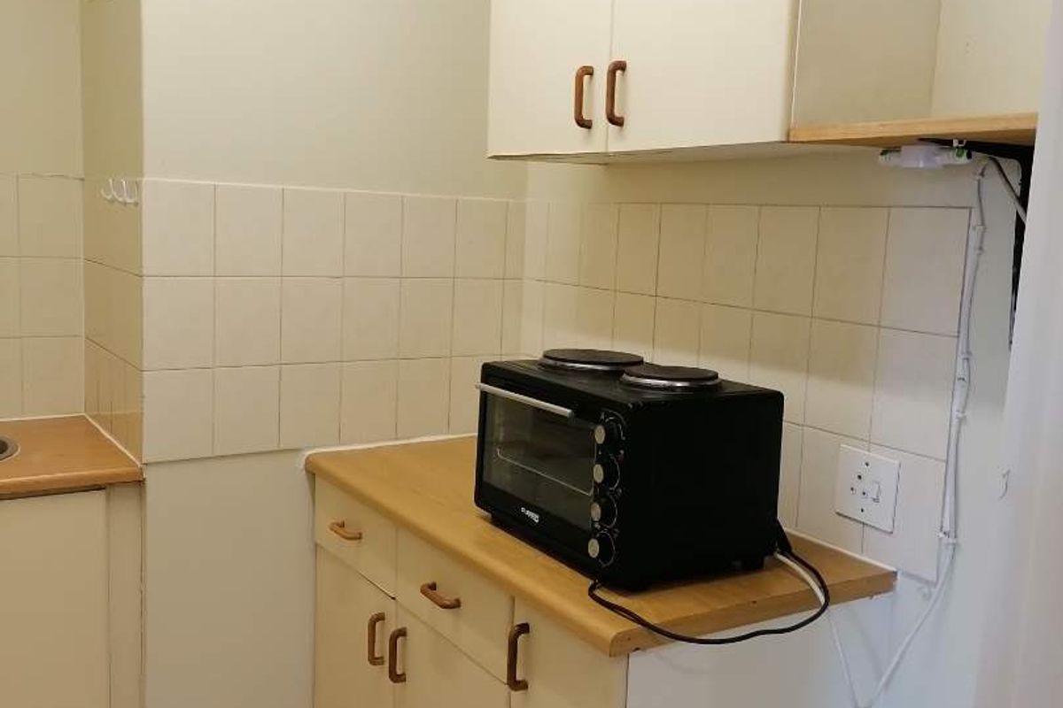 A compact kitchen featuring dated cabinetry, tiled backsplash, and tiled flooring, providing a functional but basic preparation area.