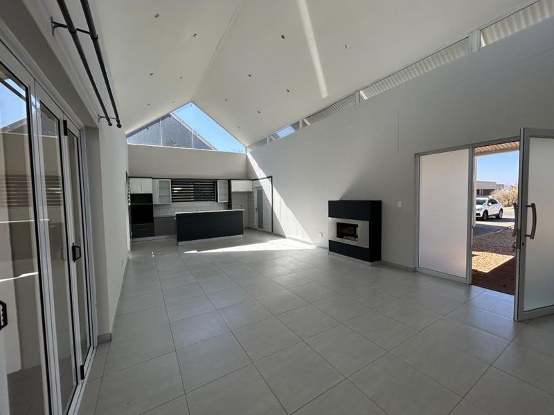 Spacious open-plan living area featuring a vaulted ceiling, tiled floors, a modern built-in fireplace, and a sleek kitchen with island.