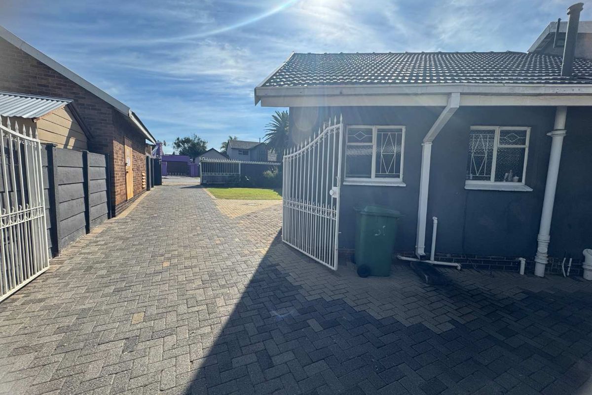A paved driveway and side courtyard area featuring a gated entrance, brick boundary walls, and exterior access to the main dwelling.