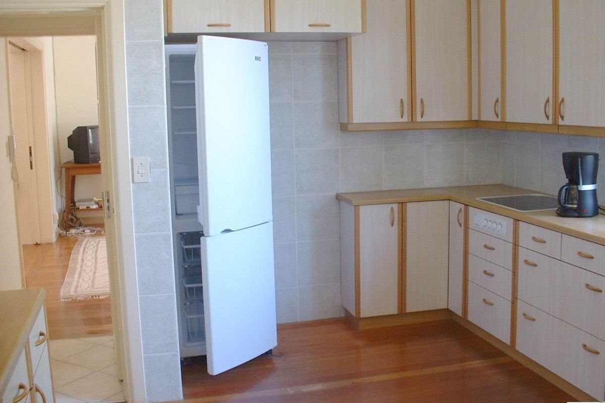 A functional kitchen featuring light-toned cabinetry, tiled splashbacks, and timber flooring, with an adjacent doorway leading to an interior living space.