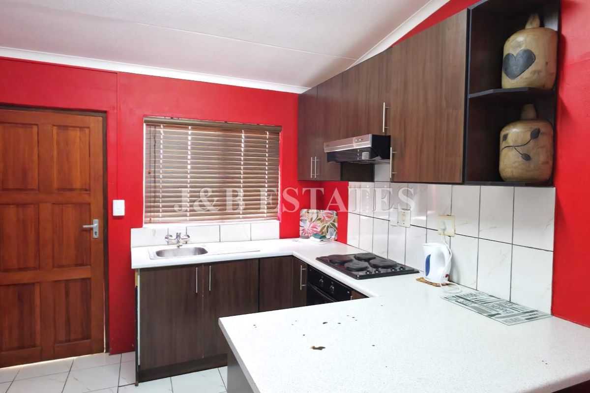 A functional kitchen featuring dark wood cabinetry, a built-in hob, extractor fan, and a stainless steel sink with tiled splashbacks.