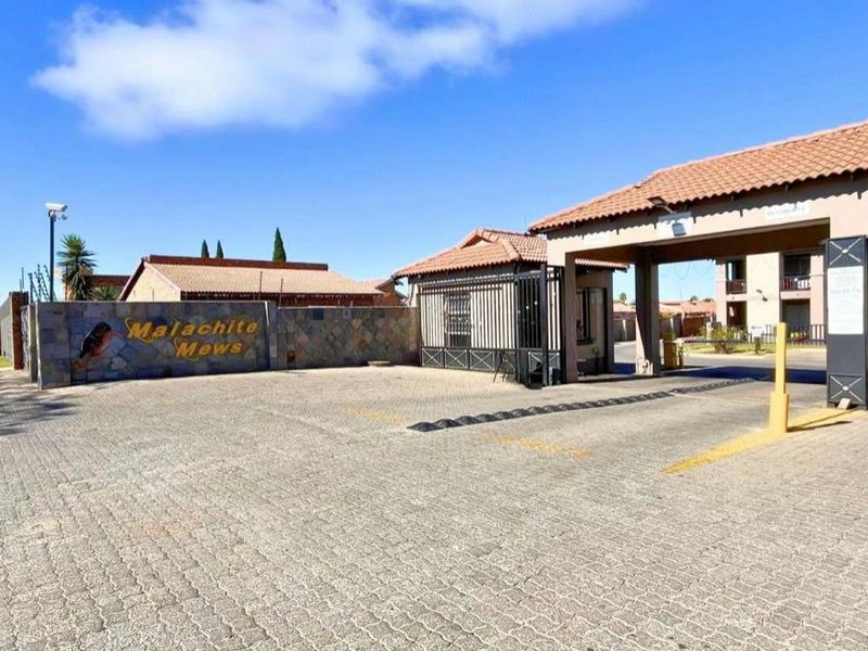 The entrance to Malachite Mews apartment complex, featuring a paved driveway, security boom gate, and stone-clad signage wall.
