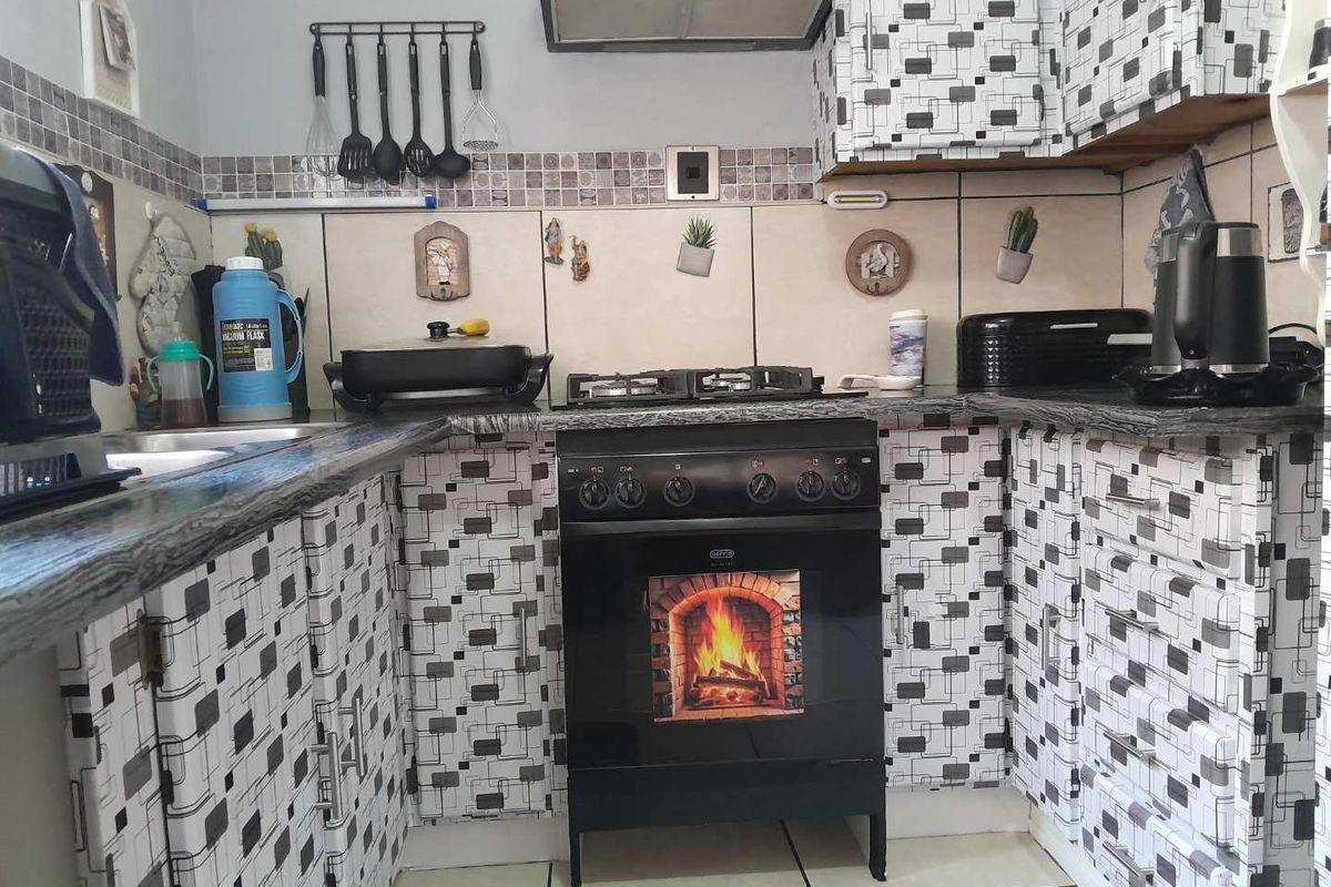 Compact kitchen featuring a gas stove, extractor fan, granite-look countertops, and tiled backsplash with patterned cabinetry finishes.