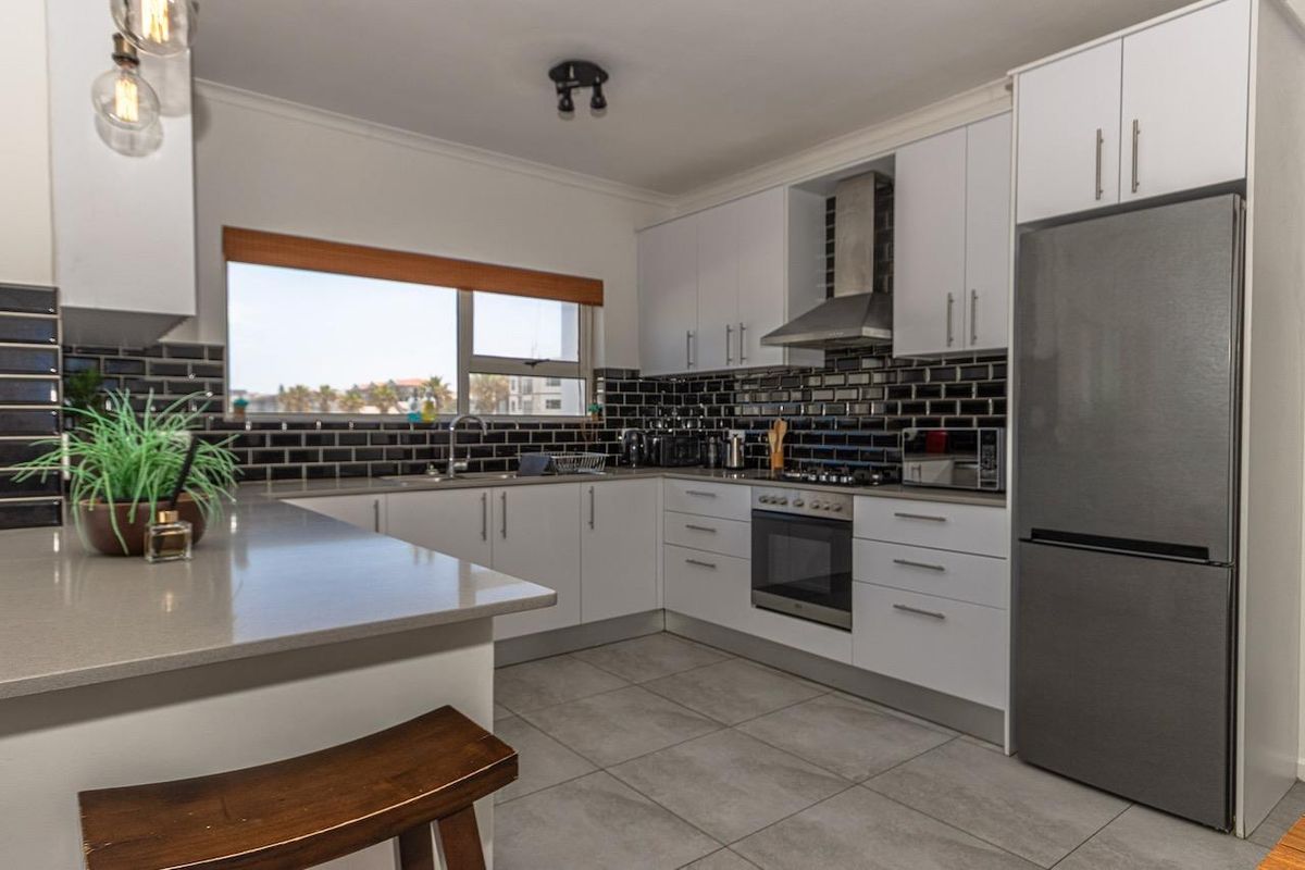 Modern kitchen featuring white cabinetry, stone countertops, black subway tile backsplash, stainless steel oven, extractor fan, and tiled flooring.