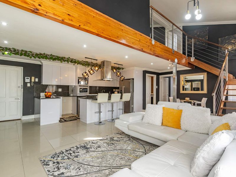 Spacious open-plan living area featuring a modern kitchen with island, sleek cabinetry, and a striking timber beam staircase leading to the upper level.