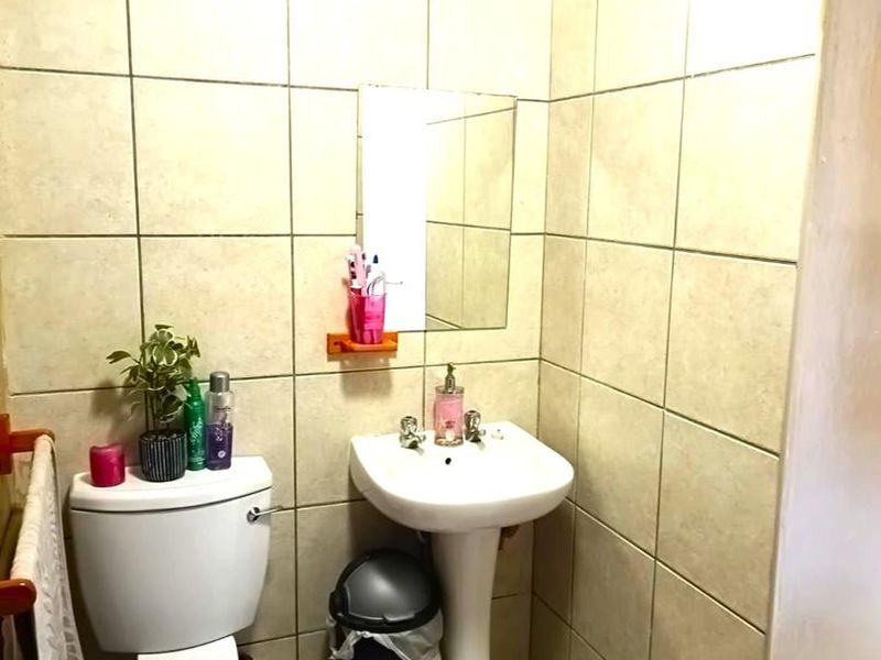 A compact bathroom featuring a pedestal basin, toilet, and neutral wall and floor tiling, requiring cosmetic updates to improve its overall condition.