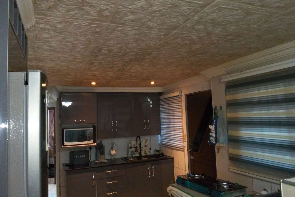A functional kitchen featuring dark grey cabinetry, black stone countertops, built-in microwave, and unique textured ceiling tiles with recessed lighting.