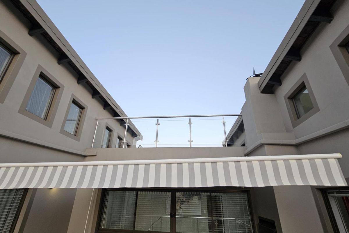 Exterior view of the property featuring a modern balcony with glass and stainless steel balustrades and a retractable striped awning over the patio area.