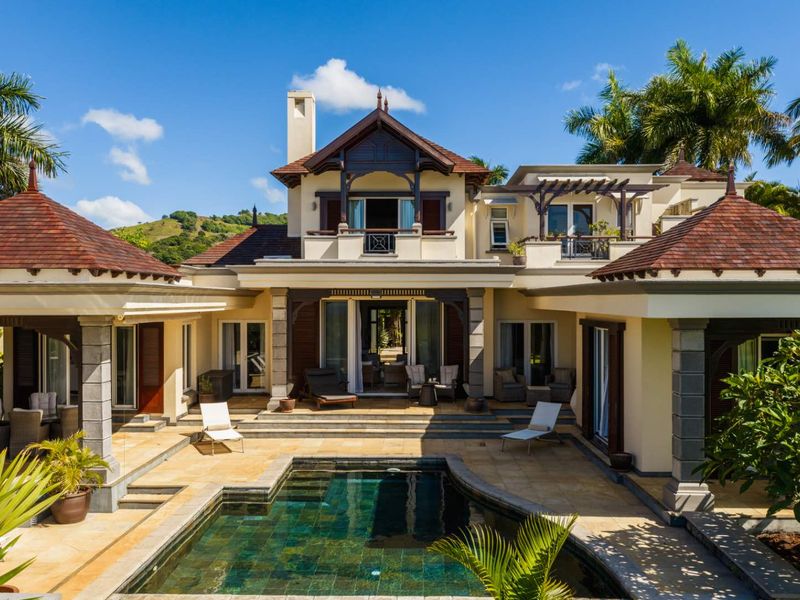 A stunning rear exterior view of a luxury residence featuring a private swimming pool, stone-paved patio, and elegant architectural detailing.