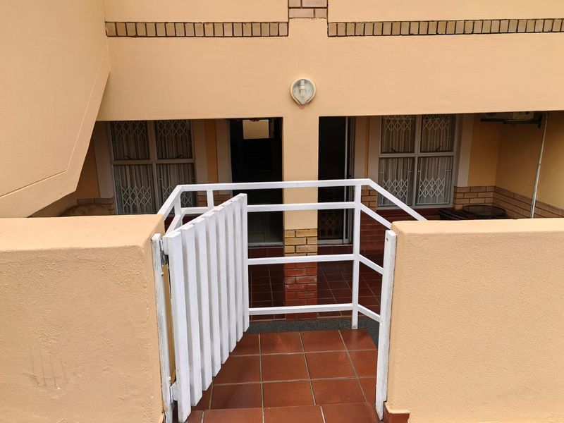 A covered patio area featuring tiled flooring, a white security gate, and security bars on the windows.