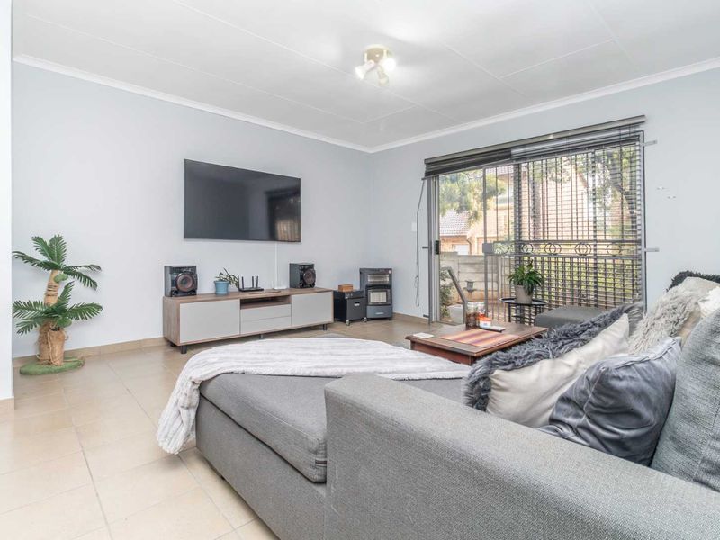 A bright living room featuring neutral tiled flooring and a large sliding glass door with security gate, providing access to the outdoor area.
