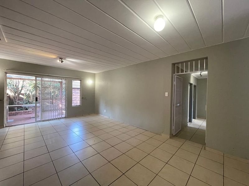 An empty, open-plan living area featuring tiled flooring, ceiling panels, and a sliding glass door providing access to the rear patio.