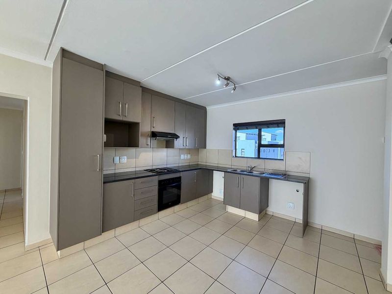 A clean, modern kitchen featuring neutral-toned built-in cabinetry, granite countertops, integrated oven and hob, and tiled flooring throughout.