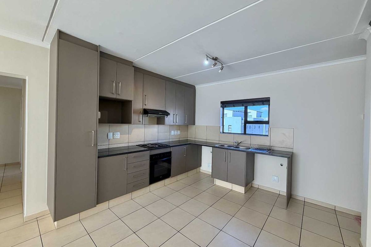 A clean, modern kitchen featuring neutral-toned built-in cabinetry, granite countertops, integrated oven and hob, and tiled flooring throughout.