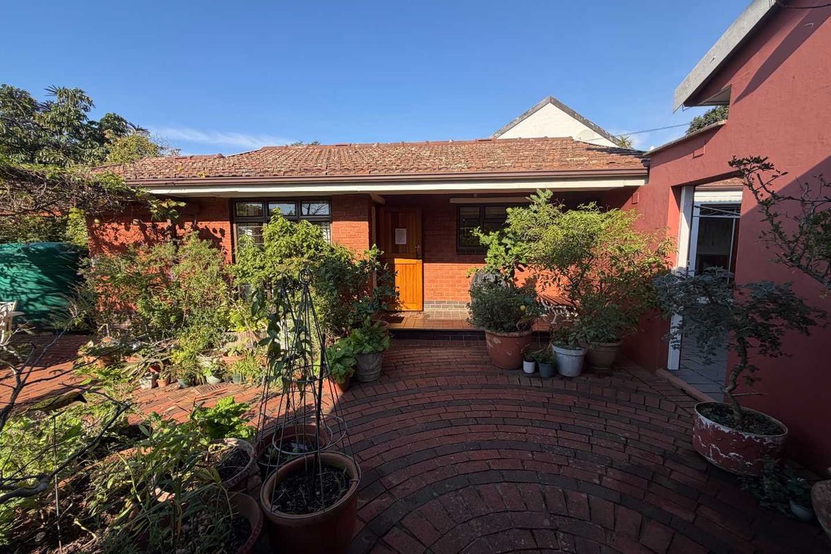 A rear view of the house featuring a red brick facade, a paved courtyard area, and a tiled roof.