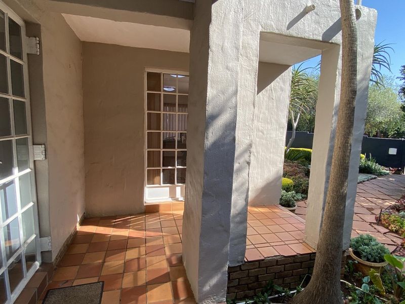 A covered patio area featuring terracotta tiling and masonry pillars, providing direct access to the garden and paved outdoor walkways.