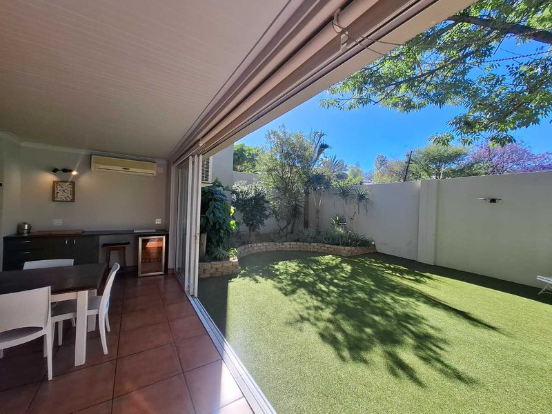 Covered patio featuring built-in cabinetry and countertop, seamlessly flowing onto a private garden area with artificial lawn and perimeter walling.