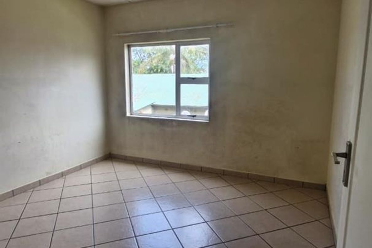 An empty bedroom featuring tiled flooring and a single window, requiring cosmetic updates to the wall finishes.