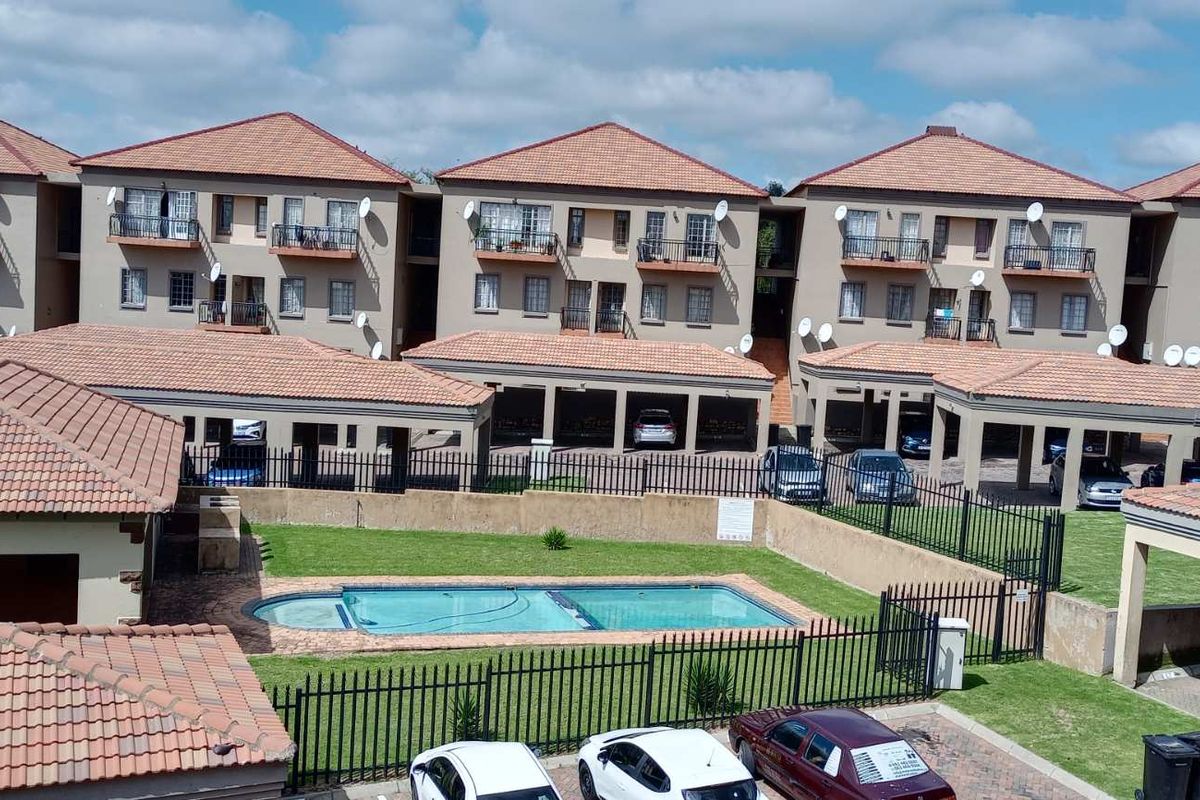 Aerial view of a townhouse complex featuring multiple residential units, a communal swimming pool, covered parking areas, and perimeter security fencing.
