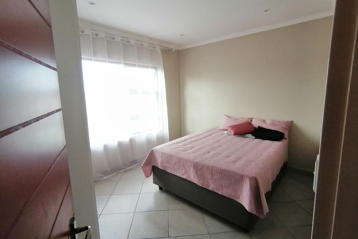A simple bedroom featuring tiled flooring, recessed downlighting, and a large window allowing for natural light.