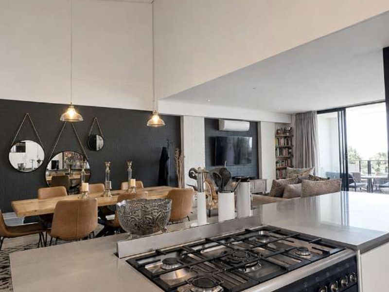Modern open-plan living area featuring a sleek kitchen with gas cooktop, stone countertops, and seamless flow to the dining space and balcony.