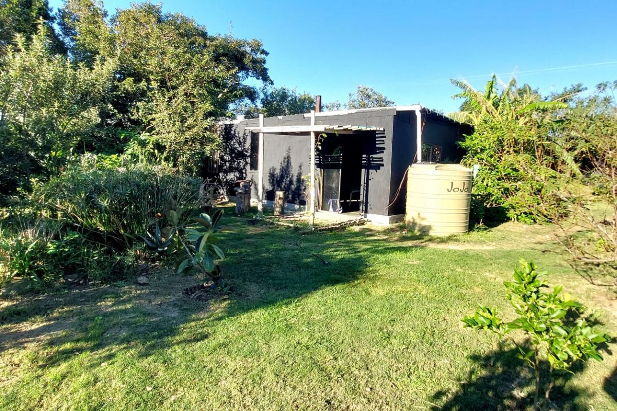 A view of a small, dark-painted structure on a residential plot, featuring a water storage tank and surrounding garden area.