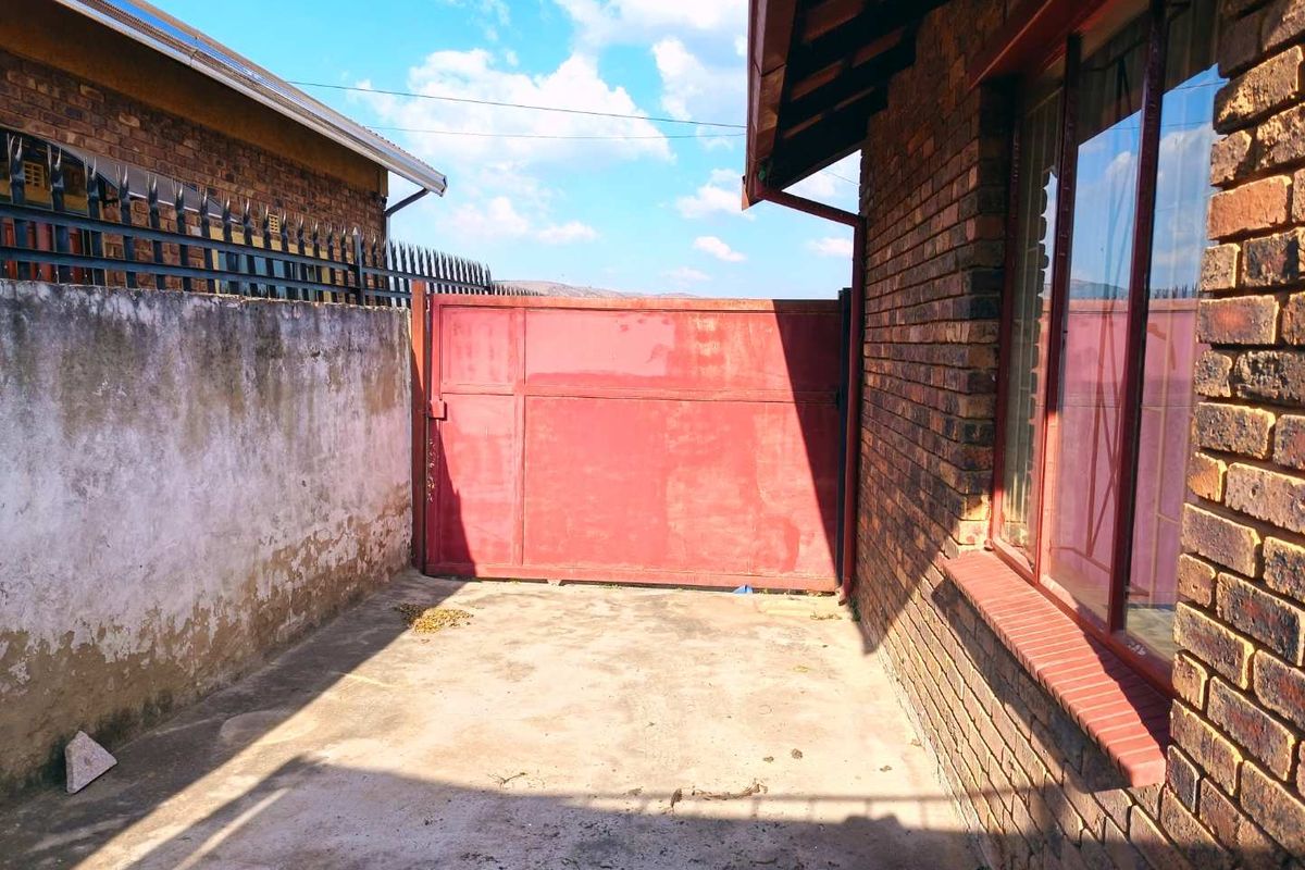 A side or rear exterior area featuring a concrete driveway, face brick walling, and a metal access gate.