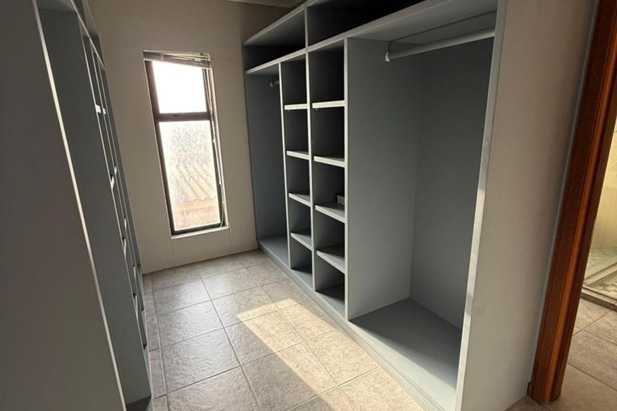 A walk-in dressing room featuring extensive built-in cabinetry, tiled flooring, and natural light from a vertical window.