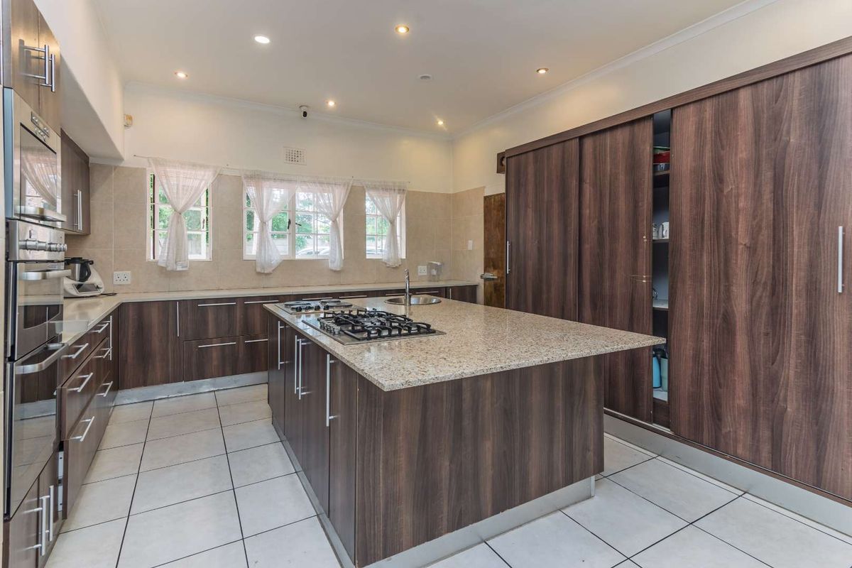 Modern kitchen featuring dark wood cabinetry, granite countertops, a central island with a gas hob, and integrated appliances.