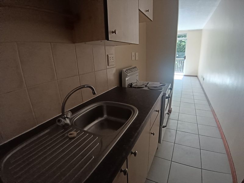 A compact, functional kitchen featuring tiled flooring, a stainless steel sink, and built-in cabinetry, leading directly into an open-plan living area.