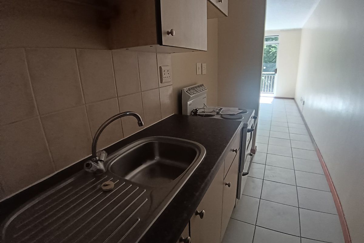 A compact, functional kitchen featuring tiled flooring, a stainless steel sink, and built-in cabinetry, leading directly into an open-plan living area.