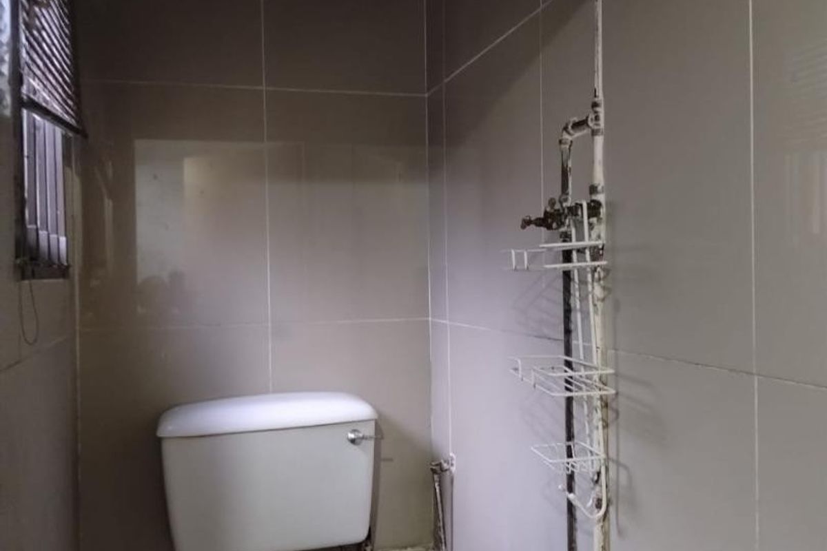 A compact bathroom featuring tiled walls, a wall-mounted basin, and a toilet, with visible exposed plumbing and dated fixtures.