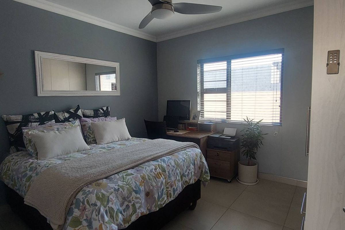 A well-maintained bedroom featuring tiled flooring, a ceiling fan, and neutral grey walls, offering a comfortable and functional living space.