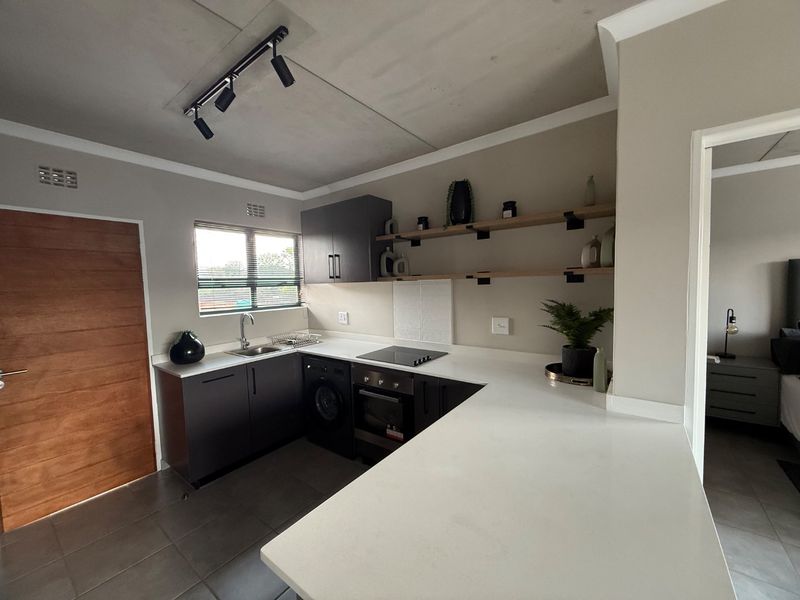Modern kitchen featuring dark cabinetry, stone countertops, integrated electric hob and oven, open shelving, and tiled flooring with track lighting.