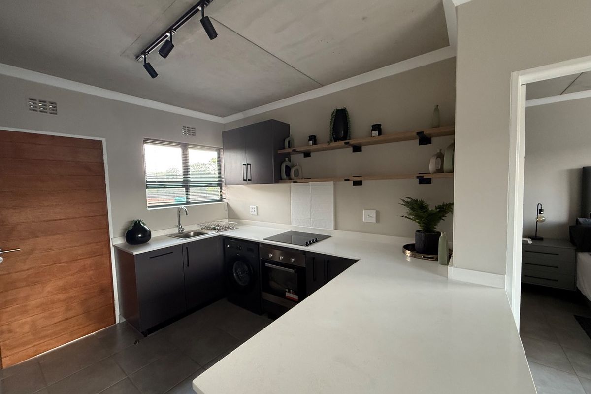 Modern kitchen featuring dark cabinetry, stone countertops, integrated electric hob and oven, open shelving, and tiled flooring with track lighting.