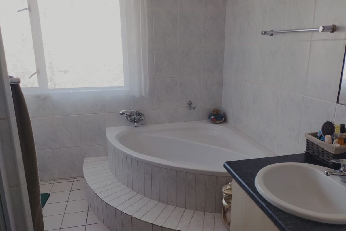 A functional bathroom featuring a raised corner bathtub with tiled surround, a vanity with integrated basin, and wall-mounted fixtures.
