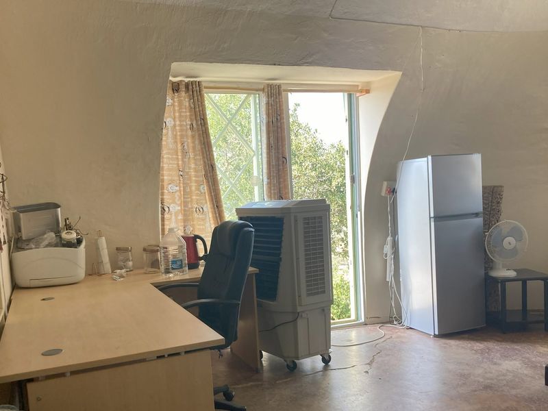 A living area featuring unique sloped walls, built-in shelving, and concrete flooring, with a window providing natural light and garden views.