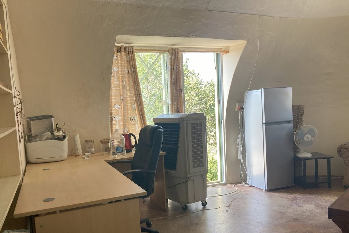 A living area featuring unique sloped walls, built-in shelving, and concrete flooring, with a window providing natural light and garden views.