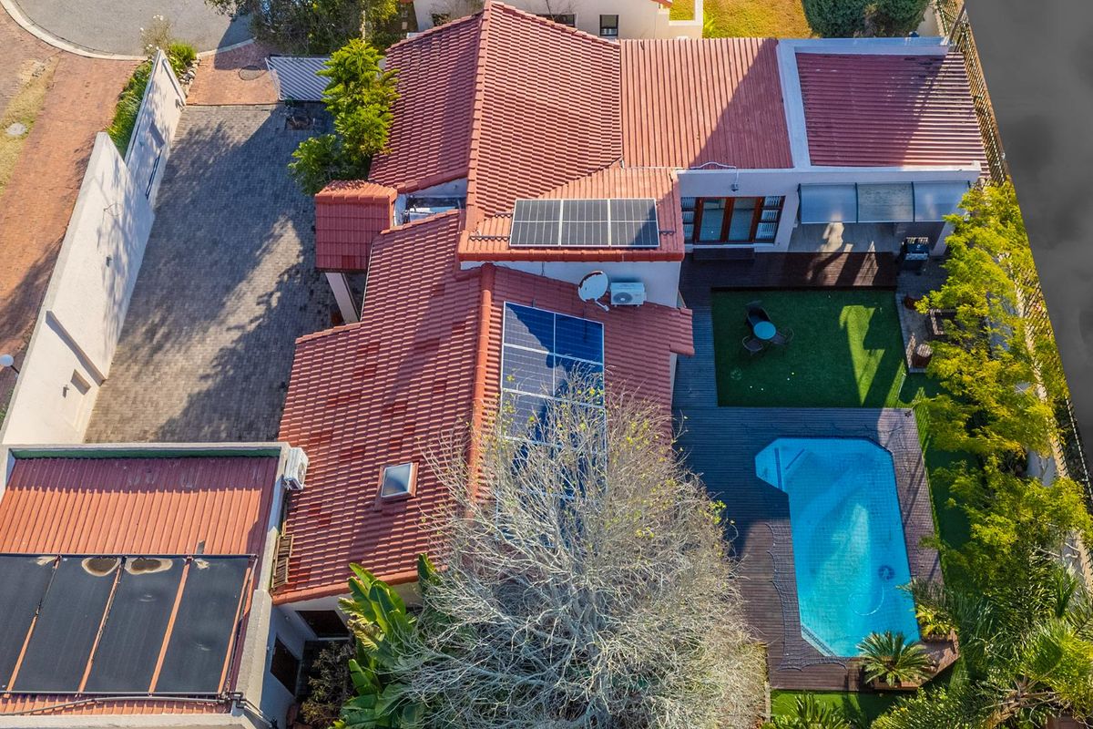 Aerial view of the property featuring a tiled roof with solar panels, a swimming pool, timber decking, and a paved driveway.