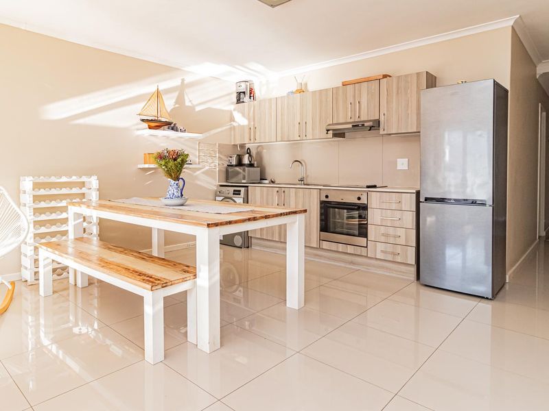 Open-plan kitchen and dining area featuring light wood-finish cabinetry, integrated appliances, and neutral tiled flooring throughout.