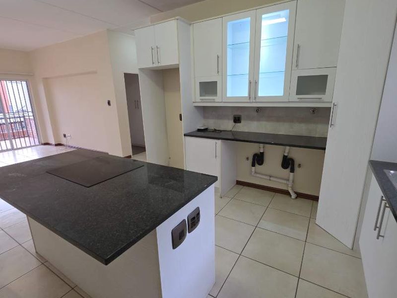Modern open-plan kitchen featuring a central island with granite countertops, white cabinetry, and tiled flooring. The space is vacant and ready for customization.
