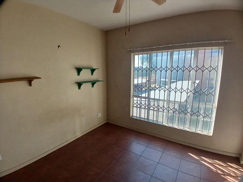 An empty bedroom featuring tiled flooring, a ceiling fan, and a large window fitted with a security gate.