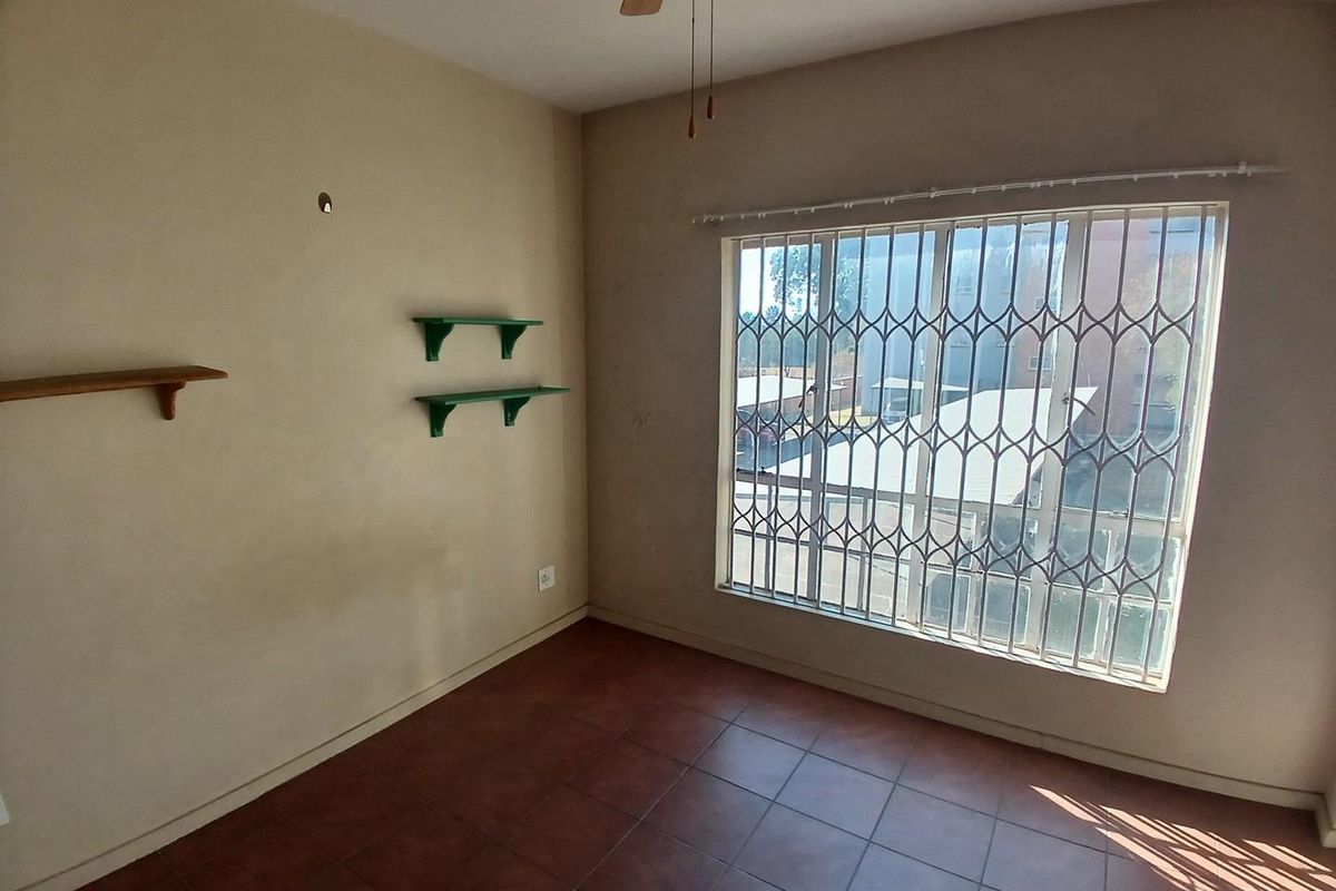 An empty bedroom featuring tiled flooring, a ceiling fan, and a large window fitted with a security gate.